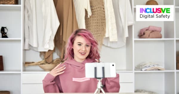 A teen with pink hair records themselves with their smartphone.