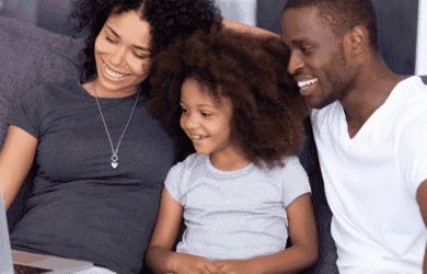 Mum, dad and daughter siting on couch smiling at laptop