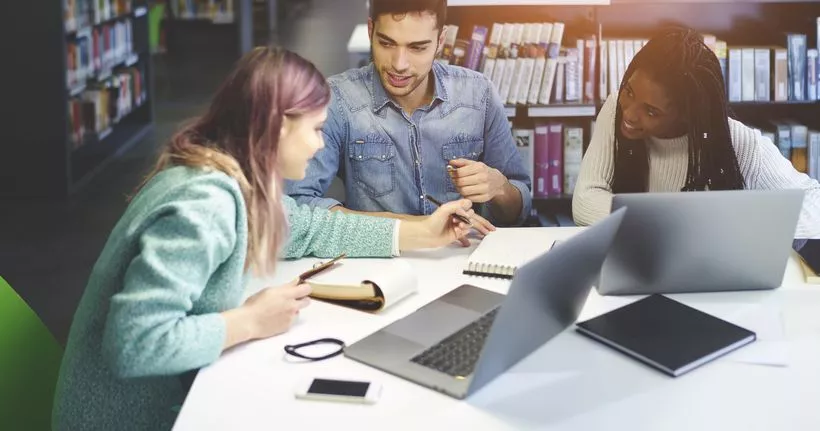 Three young adults work together with notebooks and devices.