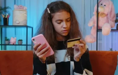A teen looks at a credit card while holding a smartphone.