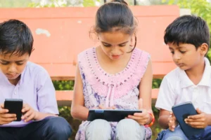 A photo shows three children sitting outside and using devices. Choosing the right apps can support wellbeing and balanced screen time.