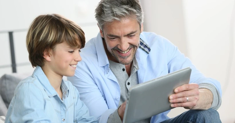 A dad uses a tablet with his son.