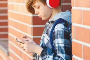 A child wears headphones and uses a smartphone.