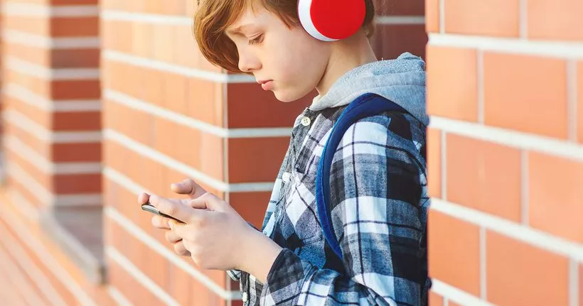 A child wears headphones and uses a smartphone.
